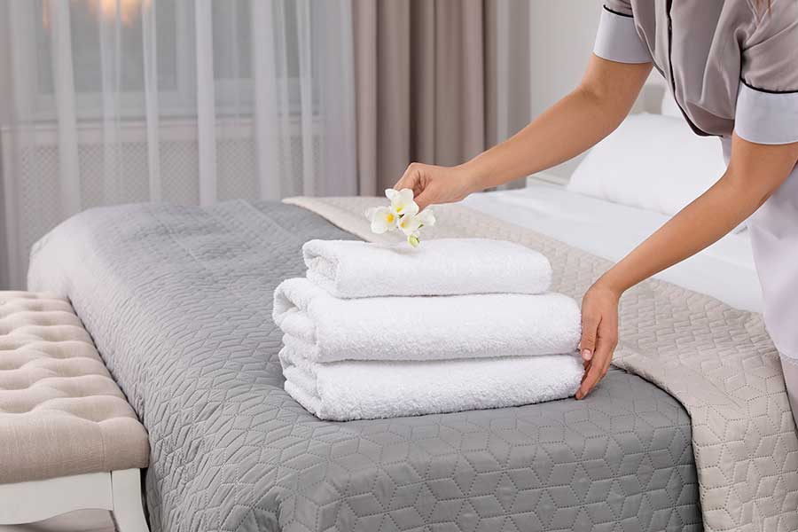 Servicemedarbejder placerer hvide håndklæder og blomst på hotelsengen